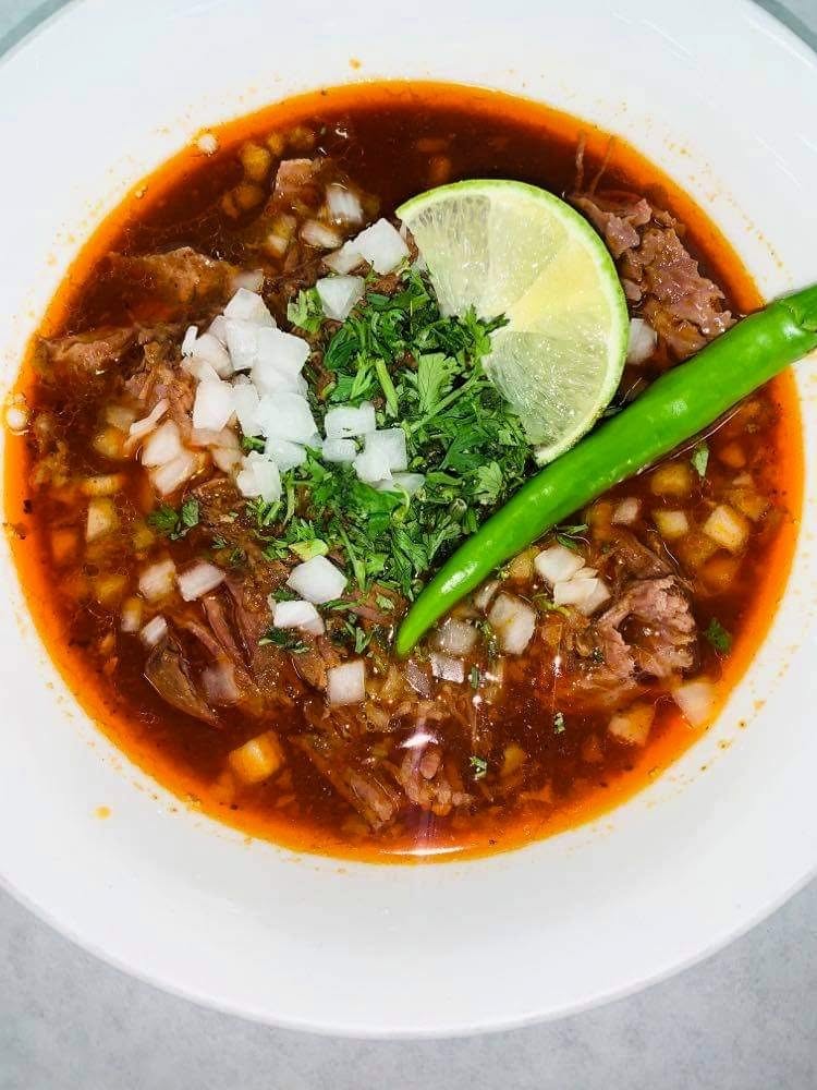 Bowl of consomé de birria with onion, cilantro and lime at Jake's Meats