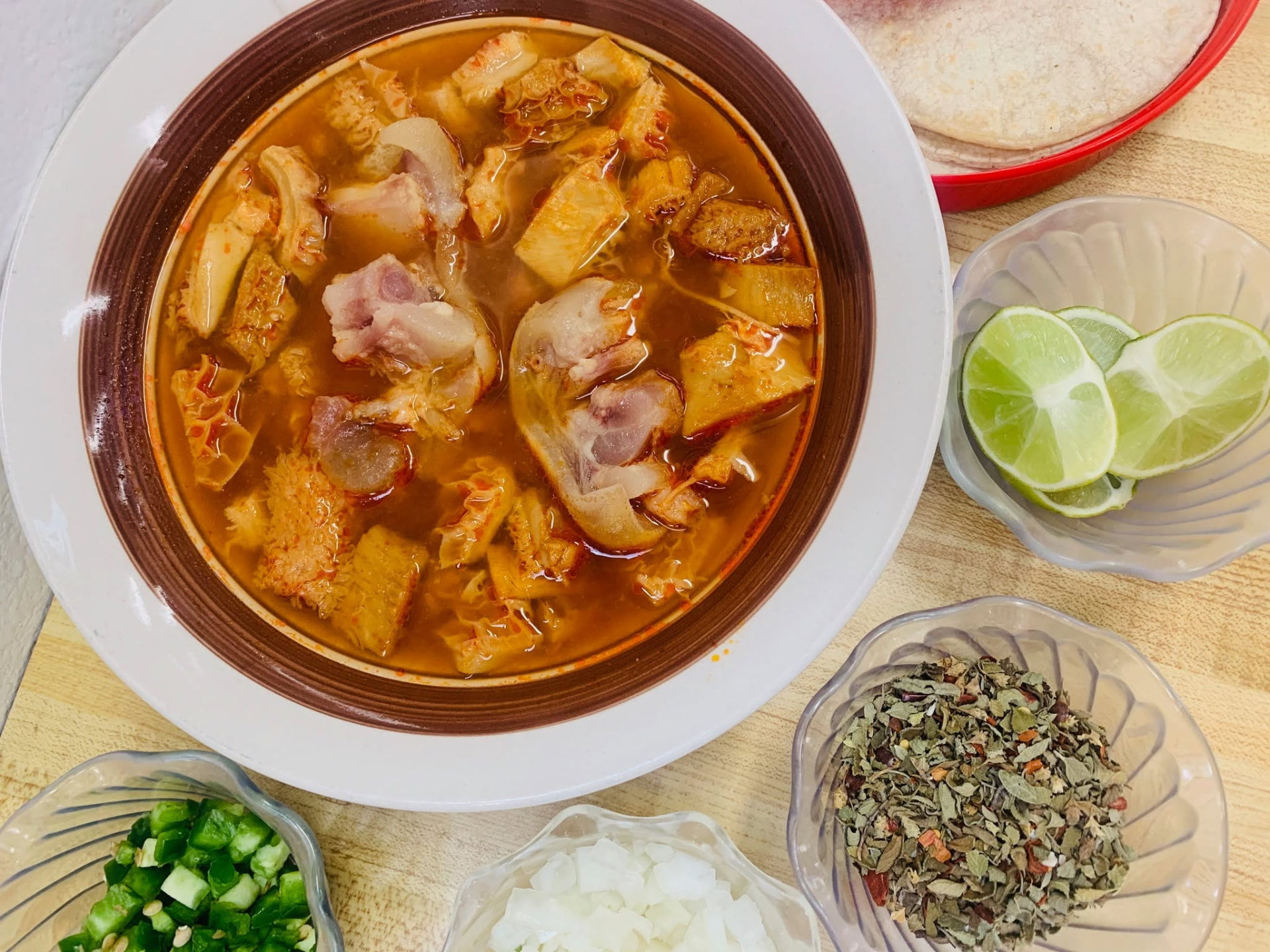 Bowl of menudo with onion, cilantro, lime and warm tortillas at Jake's Meats